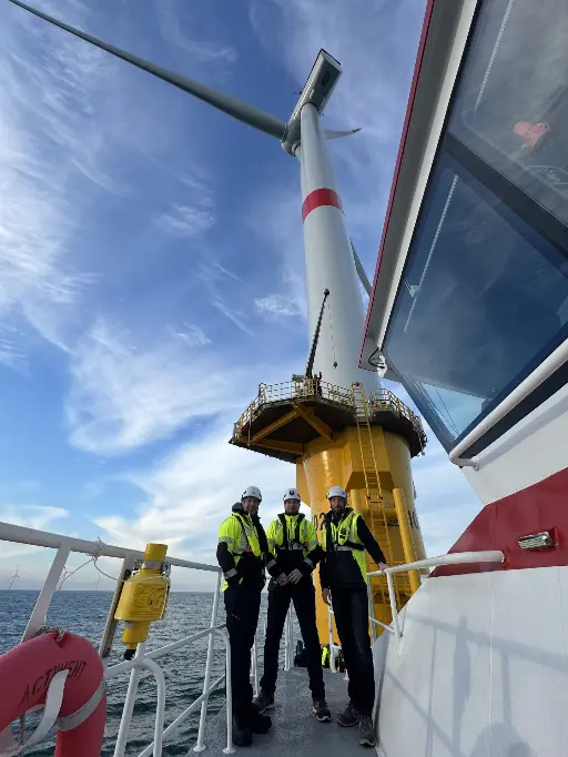 Équipe ALOTECH devant une éolienne offshore Trois hommes devant une éolienne offshore
